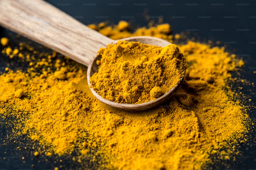 Spoonful of turmeric powder beside a cup of tea and fresh turmeric root on a wooden surface.