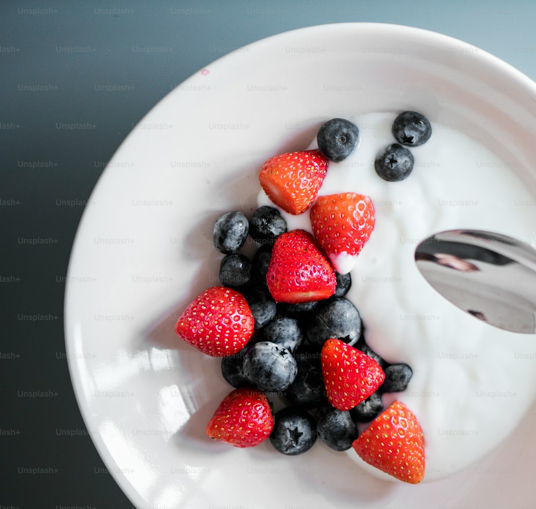 Bowl of yogurt with berries and a bottle of capsules on a bright kitchen table.